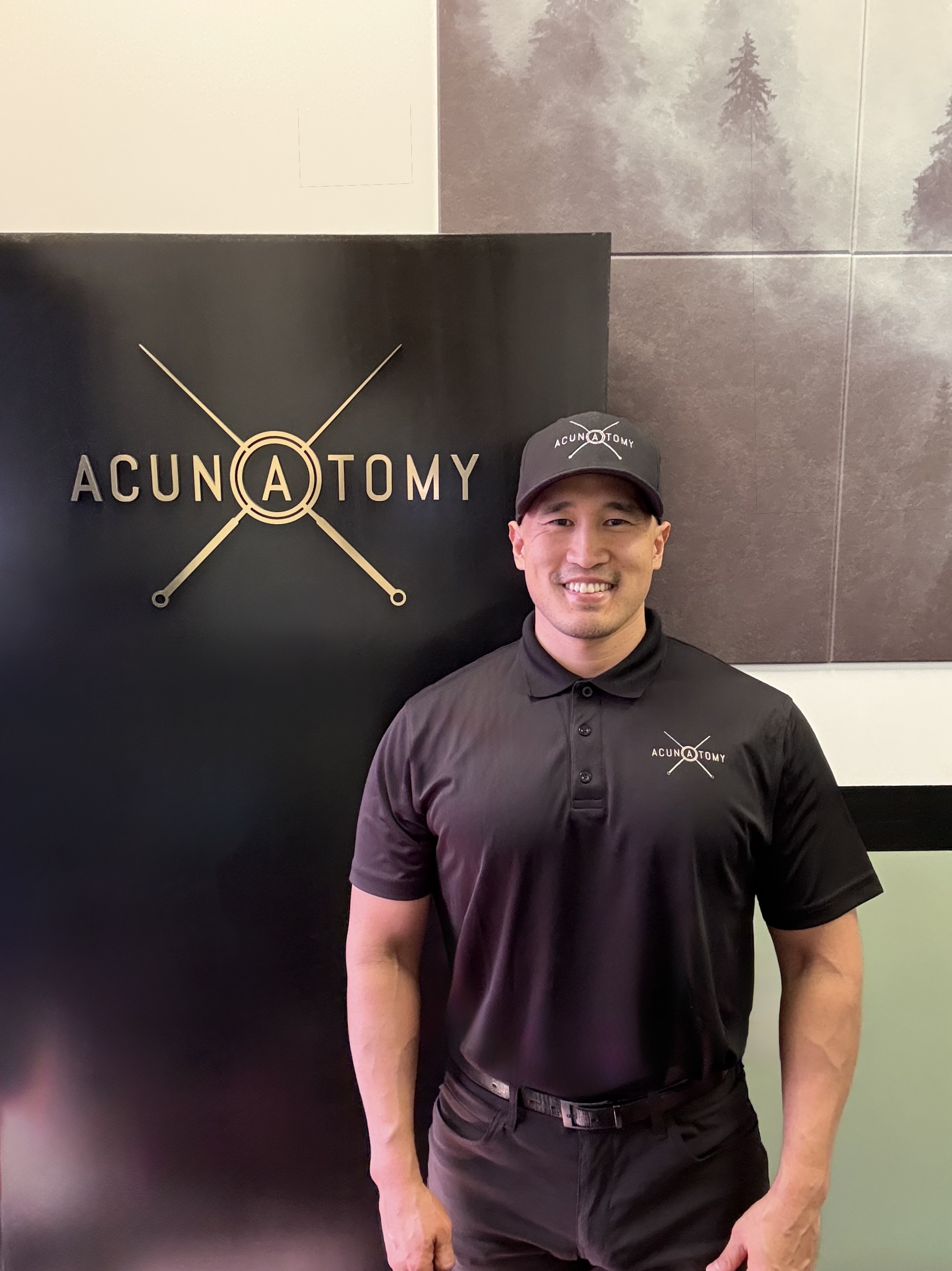 Eugene Baek, Licensed Acupuncturist, standing in front of the Acunatomy banner